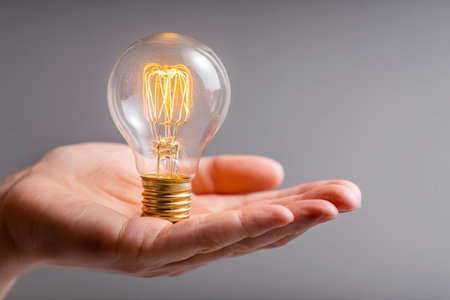 A hand gently cradles an old-fashioned bulb radiating warm light, representing fresh insights, ingenuity, and the spark of inventive energy on a simple backdrop.の写真素材