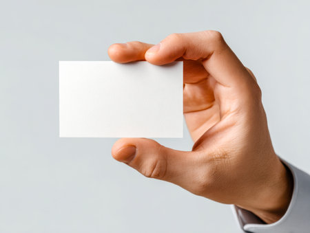 A modern professional extends a pristine white card between fingertips against a subtle gray backdrop, ideal for showcasing corporate identity or personal details with elの写真素材