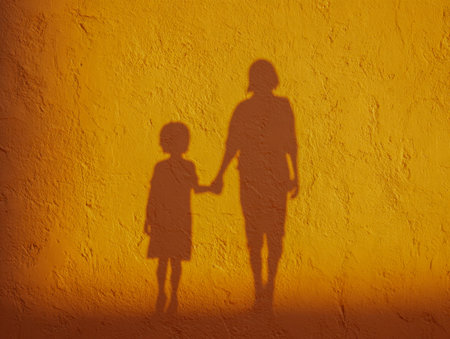 Warm sunlight creates tender silhouettes of a parent and child grasping hands on a textured yellow...