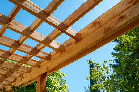 A sunlit garden scene featuring a handcrafted timber structure with a slatted roof, set among lush...
