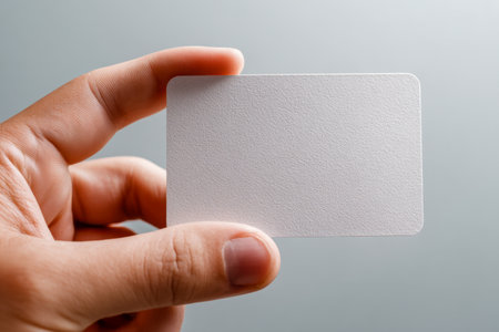 A human hand presenting a smooth, textured white card with softly rounded edges, set against a subtle gradient background ideal for branding or creative projects.の写真素材