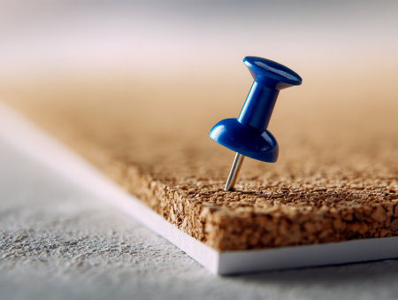 A vibrant blue pushpin embeds firmly into a cork surface, with a softly blurred backdrop evoking themes of organization and workspace efficiency.の写真素材