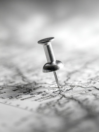 A close-up of a shiny silver pin puncturing an aged monochrome map, highlighting intricate city and road labels with a softly blurred backdrop.の写真素材