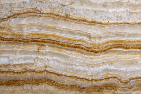 A close-up of beige and brown layered marble reveals intricate veins and organic mineral patterns,...