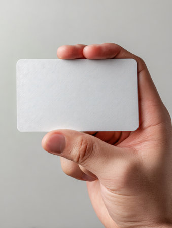 A person's hand gently presents a tactile white card with subtle texture, set against a smooth gray backdrop, ideal for customized branding or creative messaging.の写真素材