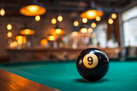 A sleek black cue ball lies on a vibrant green felt surface, surrounded by soft, warm light in a rustic tavern adorned with gentle pendant glow and inviting, intimateの写真素材
