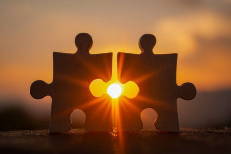 Two interlocking puzzle pieces bask in warm sunlight, set against a lively sunset backdrop, embodying harmony, strong bonds, and seamless unity.の写真素材