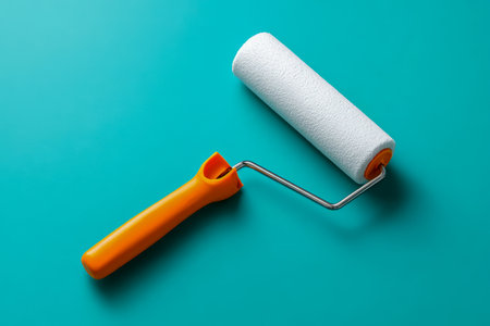 A vivid orange-handled paint roller with a soft white foam cover rests on a striking turquoise surface, evoking energy and creativity for fresh interior makeovers.の写真素材