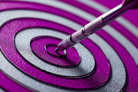A sleek metallic dart firmly embedded at the heart of a textured purple and silver target, capturing focus, mastery, and the pursuit of excellence.の写真素材