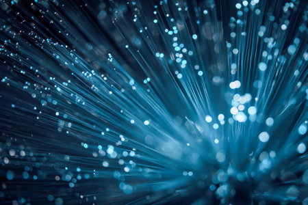 Dynamic strands of luminous fiber optics intertwine, scattering vibrant blue particles across a blurred backdrop, evoking a sleek, high-tech connectivity motif.の写真素材