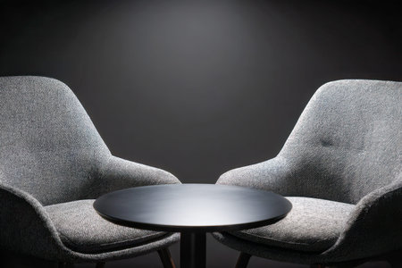 A sleek, contemporary seating area featuring two plush gray chairs flanking a compact black table,...