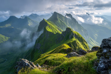 A breathtaking vista showcasing lush green mountain peaks under gentle sunlight, with swirling mist in deep valleys and towering clouds cloaking the horizon.の写真素材