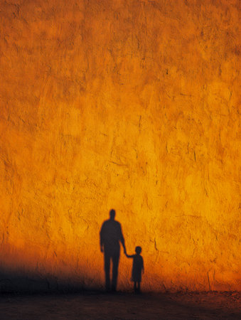 A warm, glowing silhouette of a caregiver and young one grasping hands, etched onto a rough orange surface, evoking themes of bond, guidance, and security in naturalの写真素材