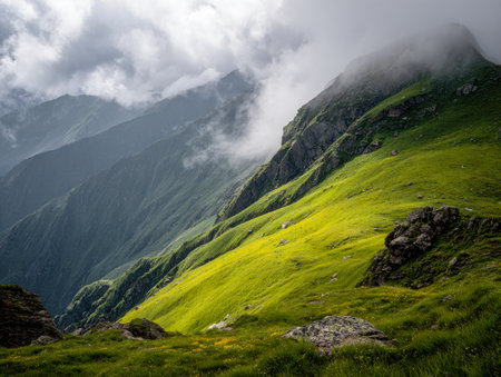 Gentle fog drifts across vibrant mountain ridges dotted with rugged rocks, illuminated by tender sunlight in a peaceful and untouched alpine wilderness.の写真素材
