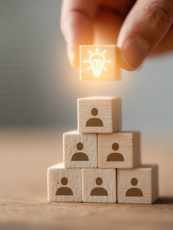 A tiered arrangement of wooden towers with human figures represents teamwork, culminating in a bright idea spotlighted by a hand, symbolizing inspiring leadership anの写真素材