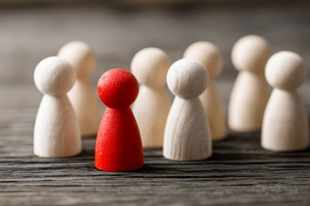 A vibrant red wooden figure commands attention amid a cluster of natural, unpainted counterparts on a weathered wooden surface, illustrating individuality and inspiring lの写真素材