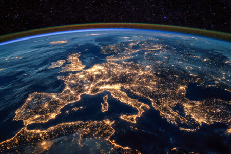 A breathtaking aerial glimpse of Europe's darkened contours lit by glowing urban hubs and shimmering coastlines under a star-studded sky, infused with a subtle atmosの写真素材