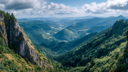 A breathtaking panorama of verdant mountains and sun-dappled valleys beneath a gently cloud-filled sky, highlighting untouched wilderness and tranquil natural splendの写真素材