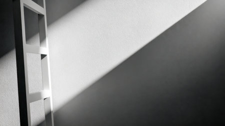 A slender white step ladder extends upward, its elongated shadow stretching across a rugged wall, illuminated by stark diagonal light that emphasizes simple geometriの写真素材