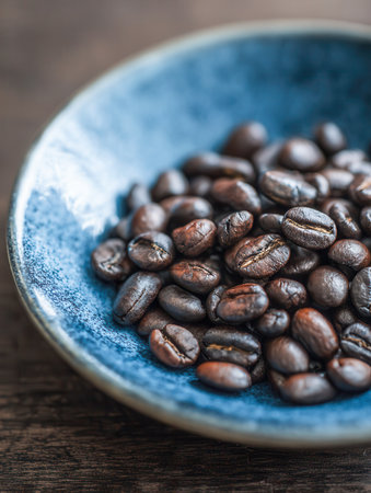 Vibrant azure ceramic bowl filled with rich, glossy coffee beans resting on warm wooden planks, illuminated by natural light that emphasizes their intricate surfaceの写真素材