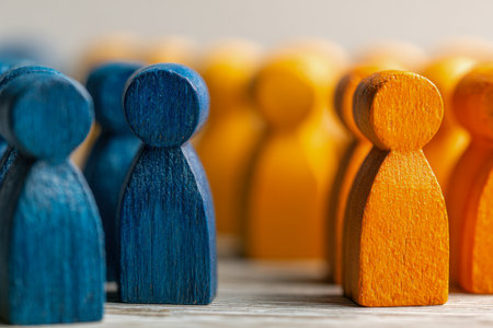 Two painted wooden figures, one blue and one orange, stand opposite each other on a weathered surface, embodying unity and effective dialogue between diverse teams.の写真素材