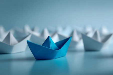 A striking blue paper vessel catches the eye among a sea of white origami boats, all gently reflected on a glossy surface beneath a calming blue hue.の写真素材