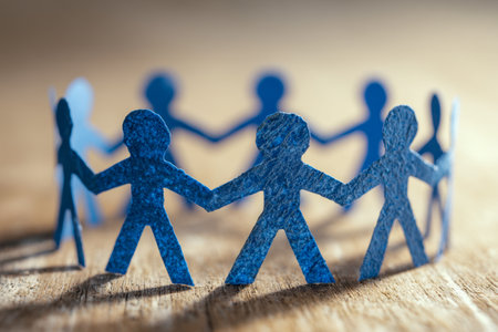 A formation of vibrant blue paper silhouettes interconnected in a loop, symbolizing collective effort and harmony, set against a warm wooden backdrop with gentle ambの写真素材