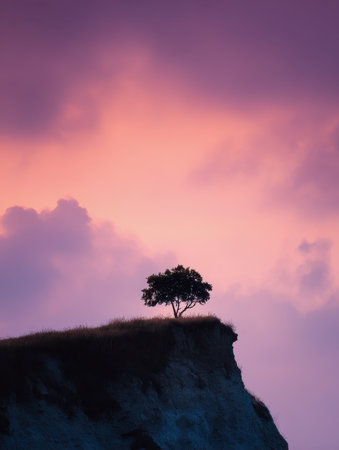 A solitary tree perches atop jagged cliffs as a fiery sunset paints the sky in shades of pink and purple, evoking both serenity and awe in nature's grandeur.の写真素材