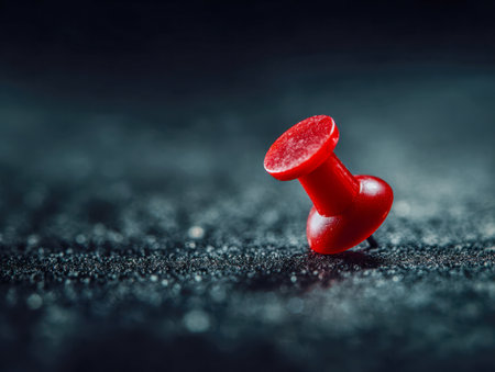 A vibrant red pin anchors focus on a rugged dark backdrop, with a blurred background emphasizing precision and organization in a creative workspace.の写真素材