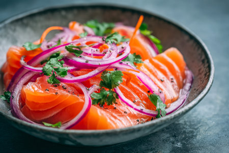Brightly colored salmon fillet slices are arranged in a rustic ceramic bowl, accented with onion...