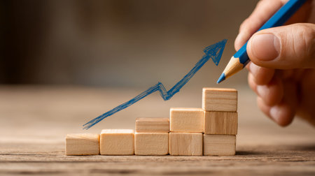 A person sketches a upward-moving arrow atop tiered wooden blocks, illustrating ongoing development,...