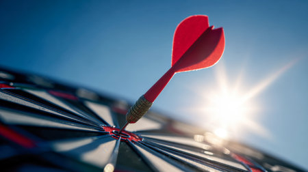 A sharply focused dart lands perfectly at the center of a vibrant target under radiant sunlight and a crisp blue sky, embodying excellence and focused determination.の写真素材