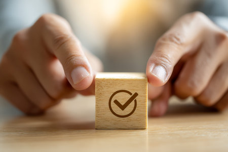 A hand gently displays a wooden tablet inscribed with a green checkmark, set against a smooth, light wood background illuminated by warm, natural light, evoking achiの写真素材