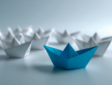 A vibrant blue paper vessel confidently navigates ahead of a fleet of pristine white boats, embodying distinction and pioneering spirit on a sleek, reflective surfacの写真素材