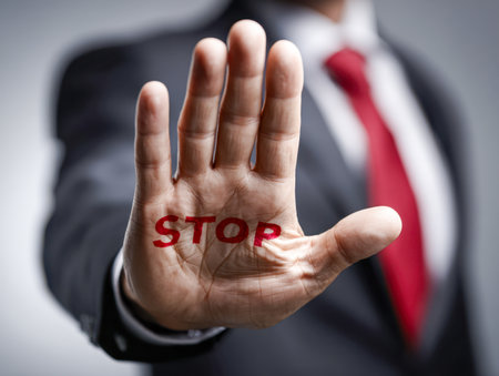 A professional man dressed in a suit and vibrant red tie gestures with his open palm, displaying a clear warning symbol on his hand to communicate caution and controlの写真素材