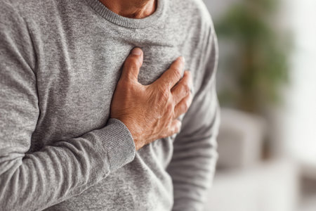 A middle-aged man in a warm gray sweater grimaces in distress, clutching his chest as gentle indoor light highlights a quiet, worried moment at home.の写真素材