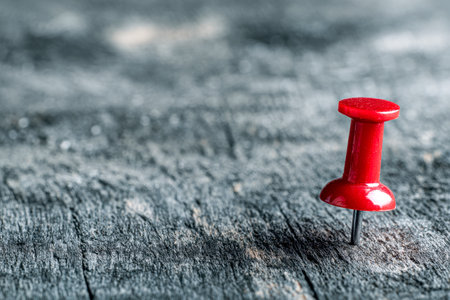 A striking crimson pin anchors a note on an aged, textured wood surface, evoking themes of focus, discovery, and thematic contrast for creative projects.の写真素材