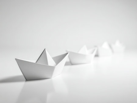 A series of pristine paper boats arranged neatly on a sleek, reflective surface against a luminous, uncluttered backdrop, evoking themes of exploration and innovationの写真素材