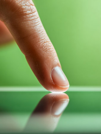 A sleek finger delicately interacts with a mirror-like surface, set against a calming, out-of-focus green backdrop in a clean, contemporary design.の写真素材