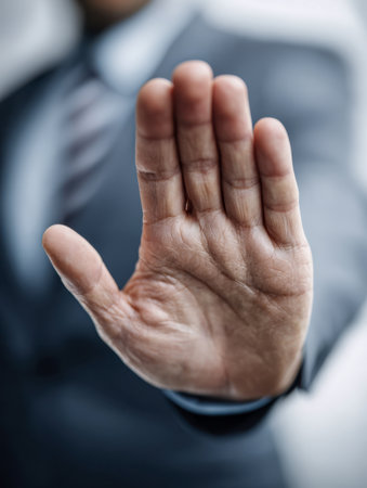 A professional in a tailored suit raises their hand with an open palm, clearly signaling a pause or boundary in a tense meeting setting.の写真素材