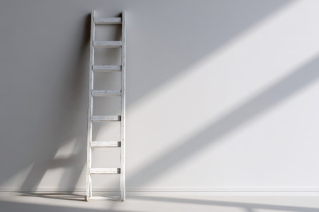 A weathered wooden ladder gently rests against a pristine white backdrop, illuminated by gentle daylight, creating serene shadows in a sleek, airy setting.の写真素材