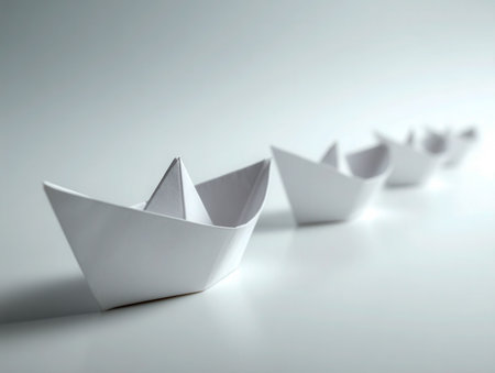 Delicate white origami vessels sit aligned on a polished surface, illuminated softly to create a gentle focus on the foremost boat, evoking calm and simplicity.の写真素材