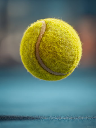 A vivid shot of a bright yellow tennis ball suspended mid-air over a textured blue court, emphasizing dynamic movement and energetic sports moments.の写真素材