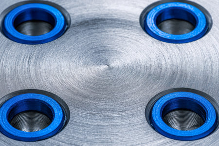 A finely crafted metal piece featuring precise concentric ridges and four symmetrically arranged blue threaded ports, highlighting expert engineering precision and sの写真素材