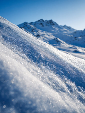 A pristine winter landscape featuring glistening snow blanketing a gentle mountain incline, with jagged summits beneath a bright azure sky on a sunny day.の写真素材