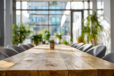 Bright, contemporary workspace featuring a spacious wooden conference table, sleek gray seating, and lush greenery accentuating the airy, natural-lit environment.の写真素材
