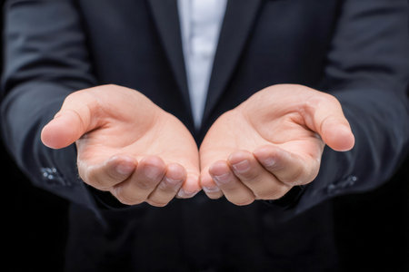 A poised professional in a sleek dark suit extends both hands forward, conveying openness, collaboration, and readiness to foster support amid a stark dark backdrop.の写真素材