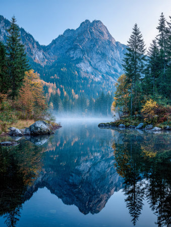 A peaceful mirror-like lake nestled among colorful fall trees and majestic mountain summits, capturing a crisp morning's stillness and vibrant wilderness essence.の写真素材