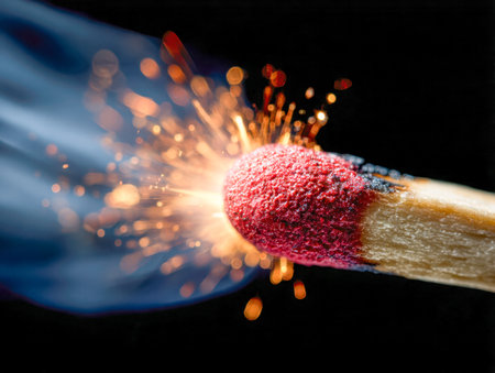 A vivid flame erupts from a matchstick, casting flickering light and glowing embers into a dark backdrop, capturing intense motion and fiery energy.の写真素材