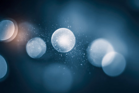 Delicate luminous spheres and shimmering specks drift across a deep blue backdrop, forming an...